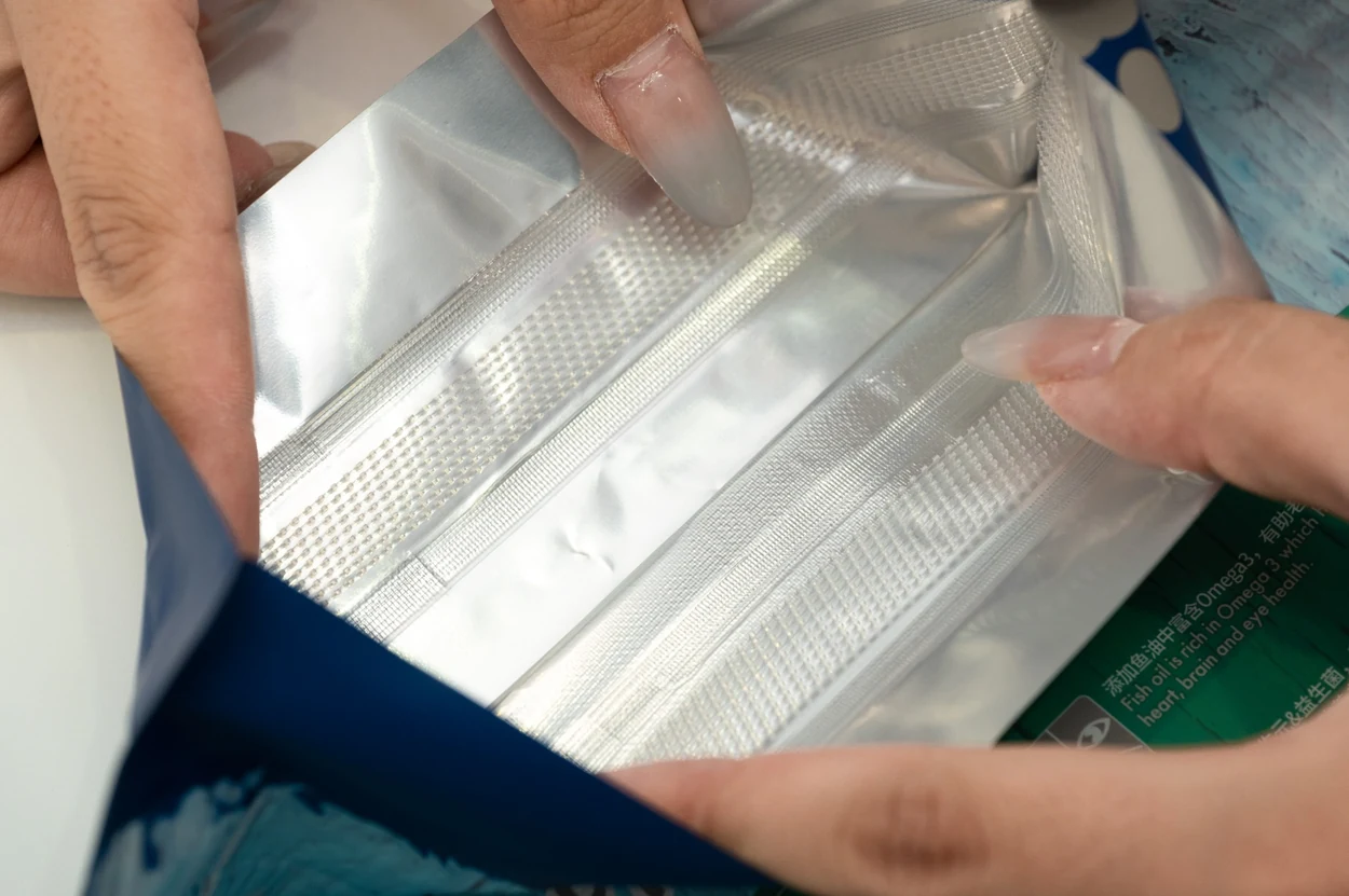 Original close-up photograph of hands holding open a pouch to show its inner film and closure area
